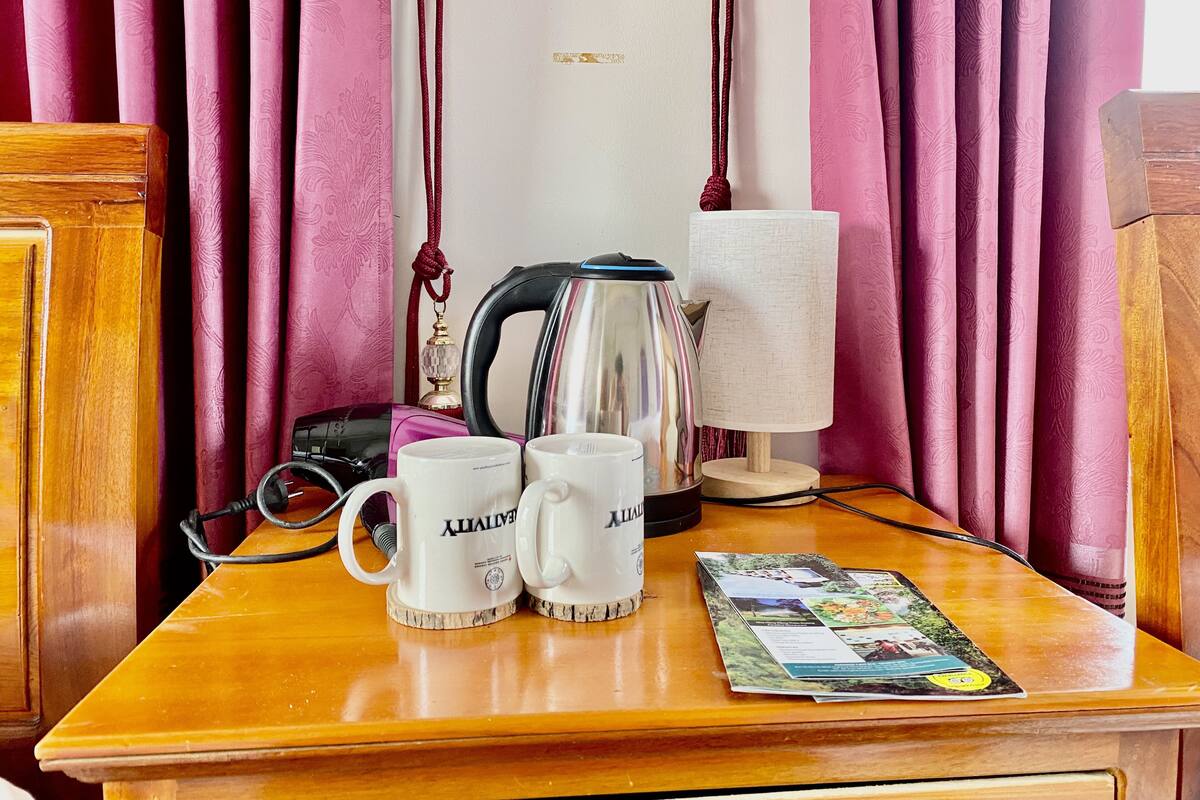 A wooden table with two white mugs, a kettle, a lamp, and a magazine.