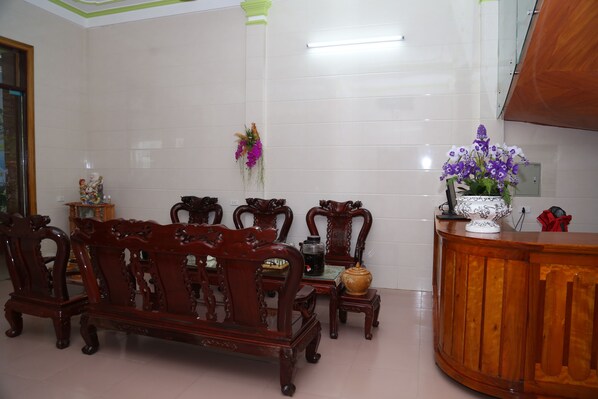 A room with a wooden bench, a small table, and a cabinet with a vase of flowers. - Tien's Cozy Homestay (Phong Nha)