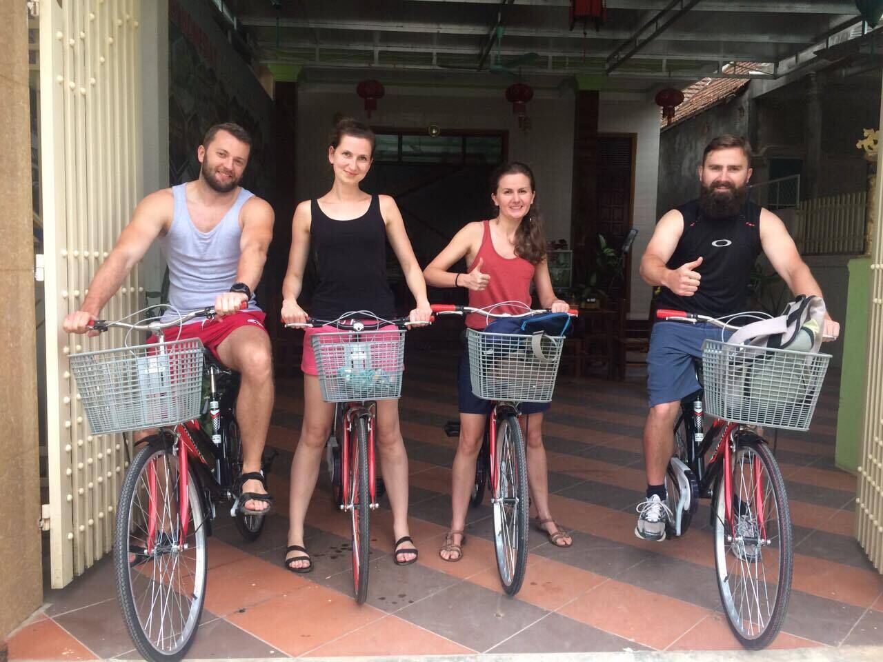 Cuatro personas en bicicleta, cada una con una cesta en el manillar, de pie en un umbral.