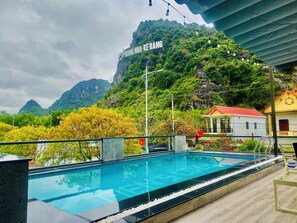 A swimming pool with a view of a mountain and a sign reading "PHONG NHÂ-KEBANG". - Tien's Cozy Homestay (Phong Nha)