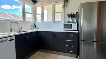 A modern kitchen with a stainless steel refrigerator, dark cabinets, a microwave, and a window with a view of the roof.