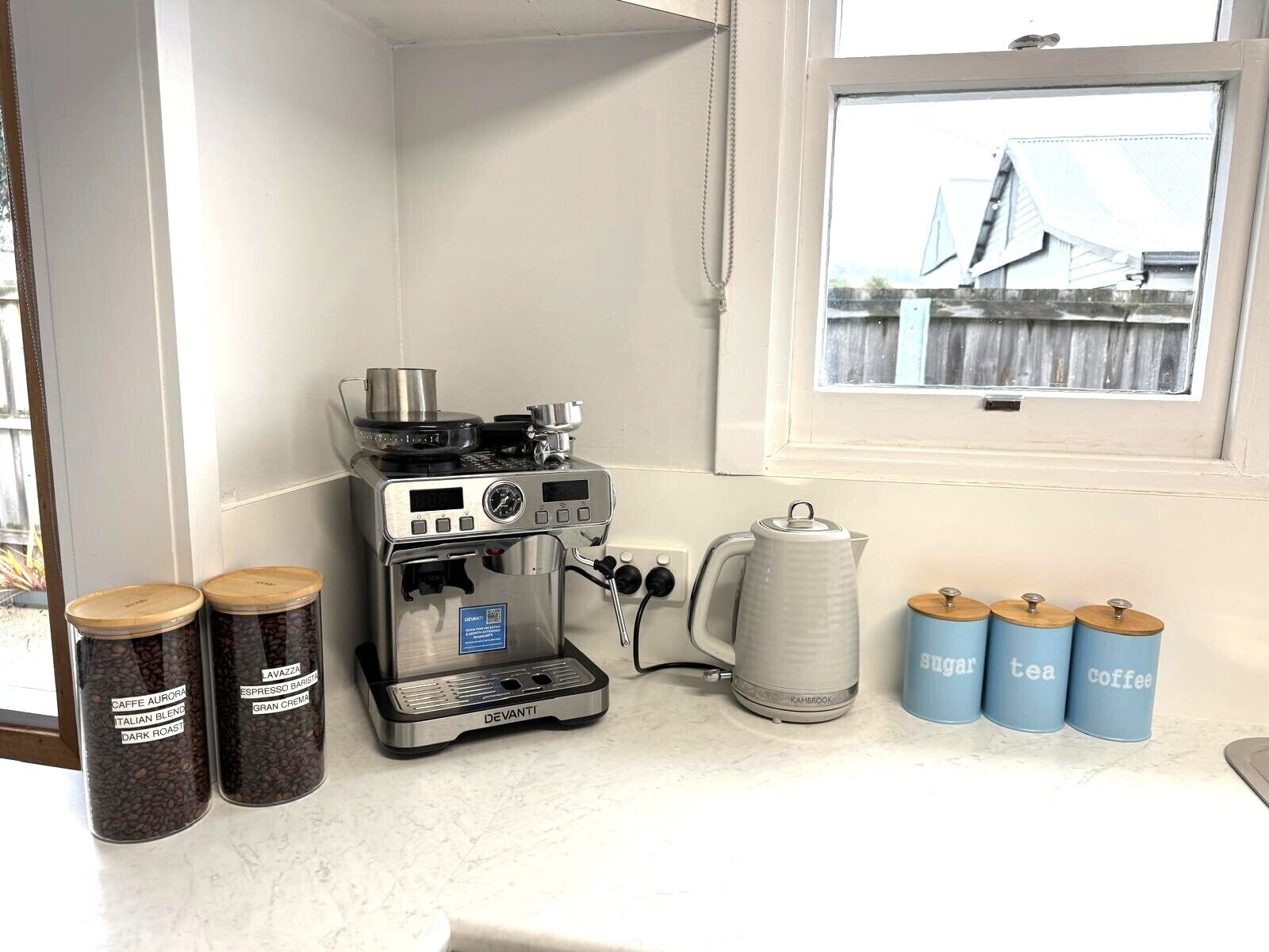 Máquina de café com recipientes etiquetados de grãos de café e chaleira.