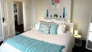A neatly arranged bedroom with a bed, bedside tables, and a wall-mounted shelf with decorative items.