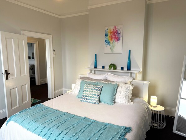A neatly arranged bedroom with a bed, bedside tables, and a wall-mounted shelf with decorative items.