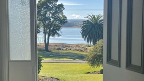 A view through a door to a grassy area with a tree and a palm tree, leading to a body of water.