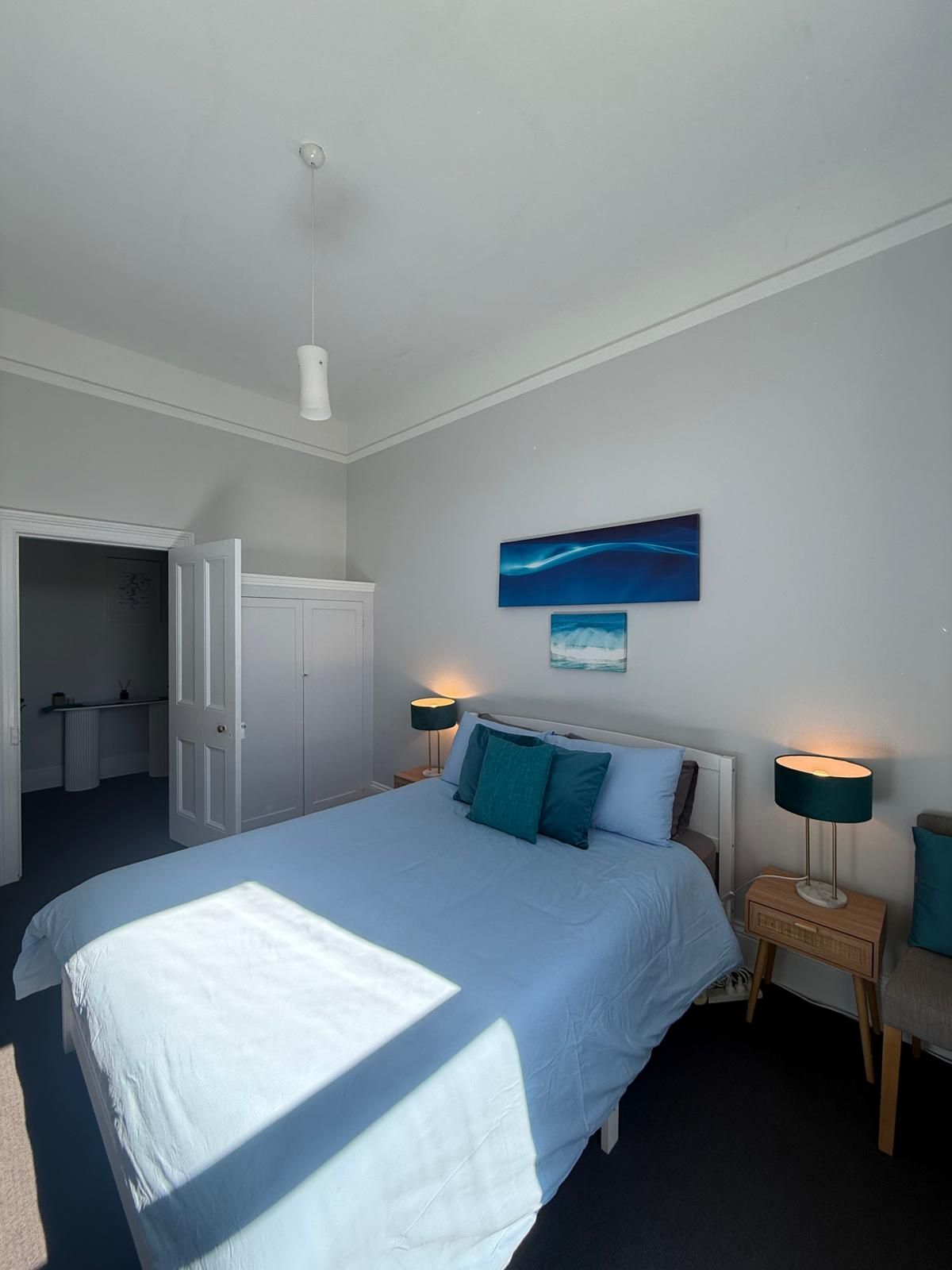 Een slaapkamer met een bed, nachtlampjes, een deur en een muur met een schilderij.