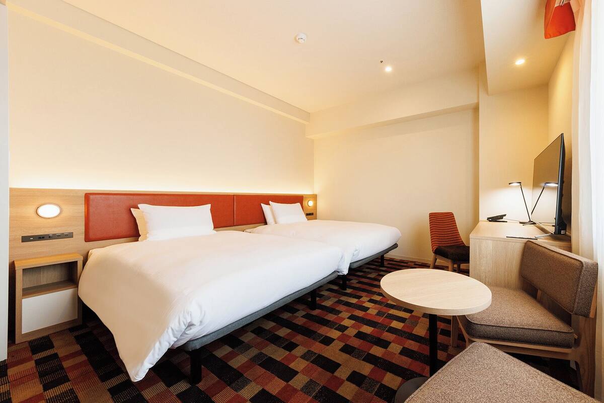 A hotel room with a large bed, a desk with a chair, a small round table, and a television.