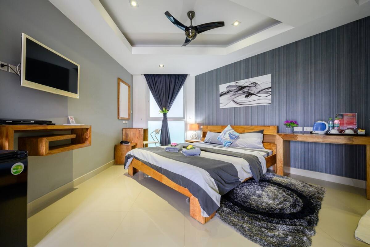 Une chambre à coucher moderne, équipée d’un lit, de tables de chevet, d’un ventilateur de plafond, d’une télévision et d’un bureau avec une chaise.