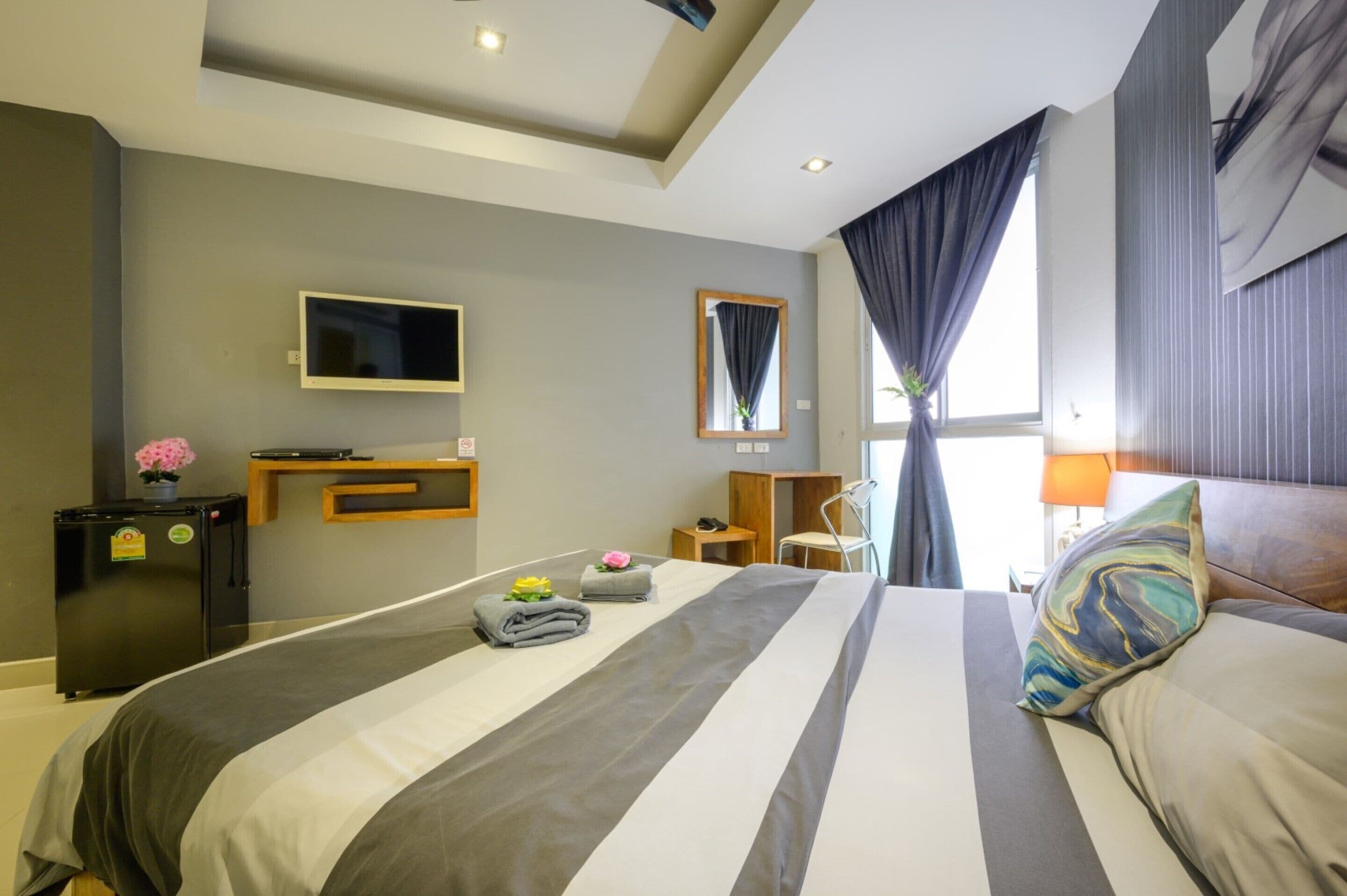 A hotel room with a large bed, a flat-screen TV, a small desk, a chair, and a window with curtains.