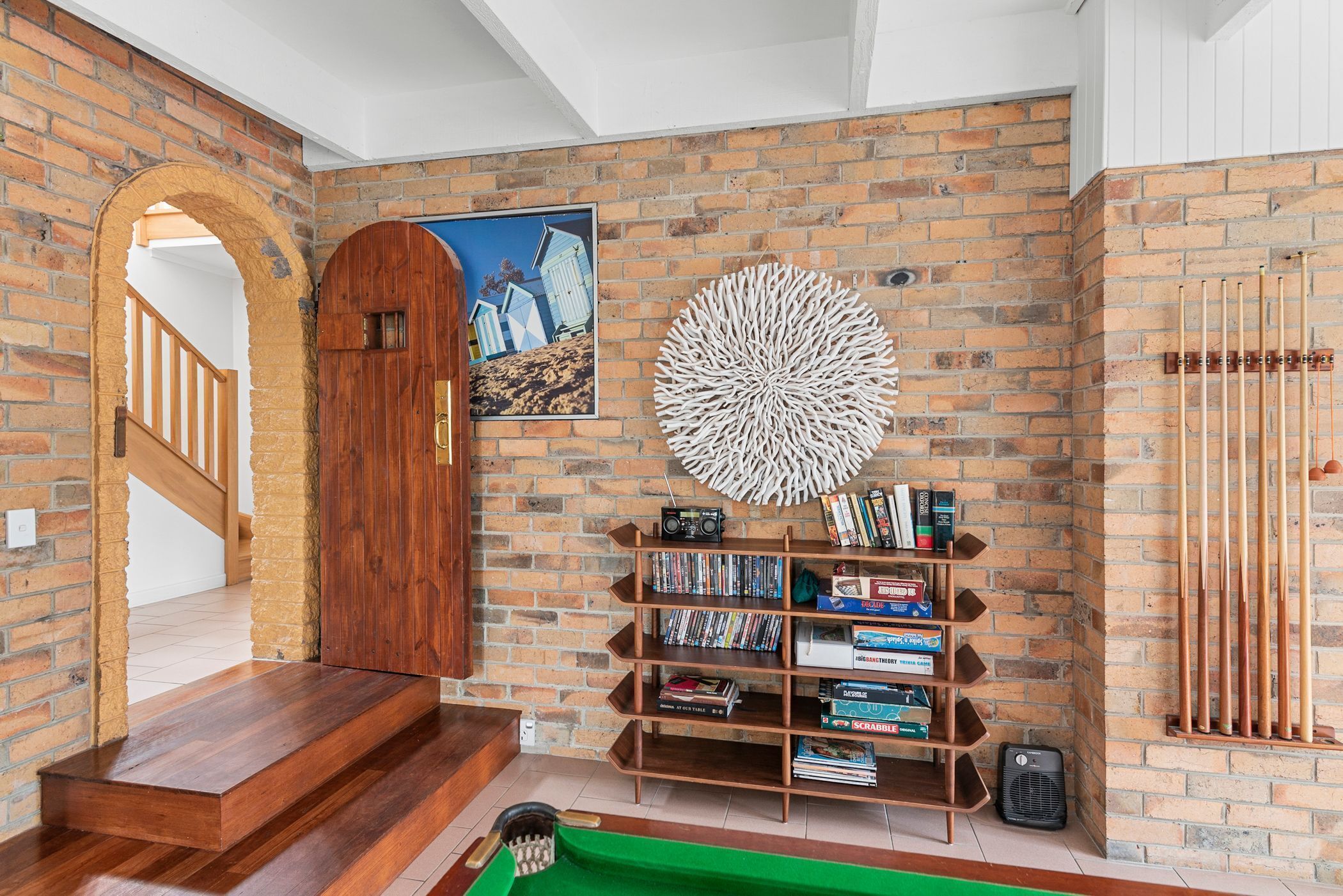 A room with a brick wall, a wooden door, a bookshelf, a billiards table, and a staircase.