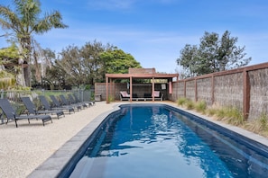 Piscina com espreguiçadeiras e um pergolado.