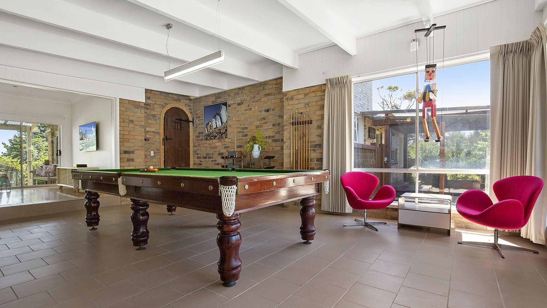 A spacious room with a pool table, a billiards rack, and a large window with curtains.