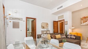 Ein modernes Wohnzimmer mit einem Glastisch, weißen Stühlen, einem braunen Sofa mit Kissen und einem gelben Sessel.