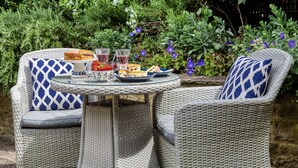 A wicker outdoor dining set with a glass table, two chairs, and a plate of food and drinks. - Rectory Cottage -  a beautiful cottage sleeping two guests (near Stamford)
