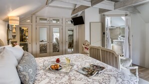 Un dormitorio con cama, mesita de noche con lámpara, televisión, armario y baño visible a través de una puerta abierta.