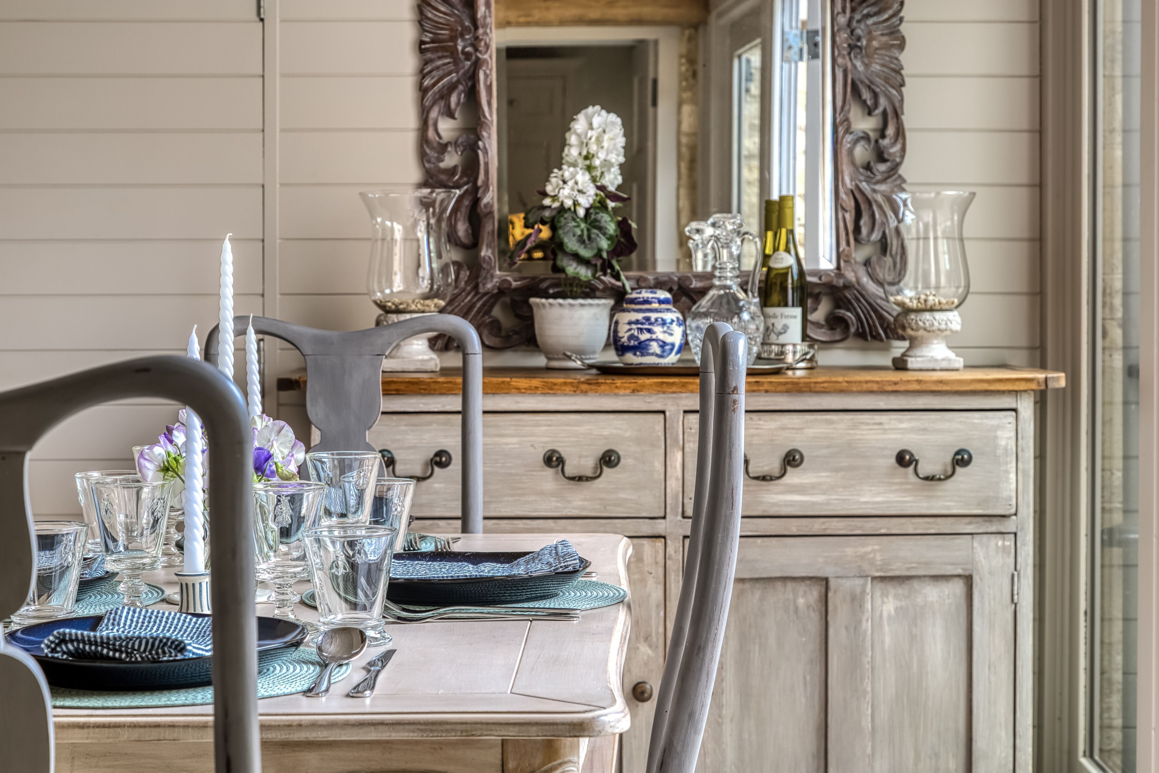 A dining table set with glassware, plates, and cutlery, a vase with flowers, and a mirror above the table.