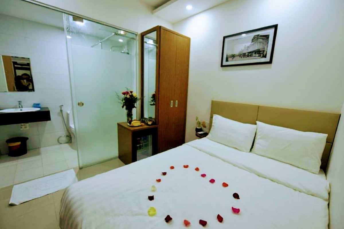 A hotel room with a bed, a bedside table, a mirror, a wardrobe, and a bathroom with a sink and shower.