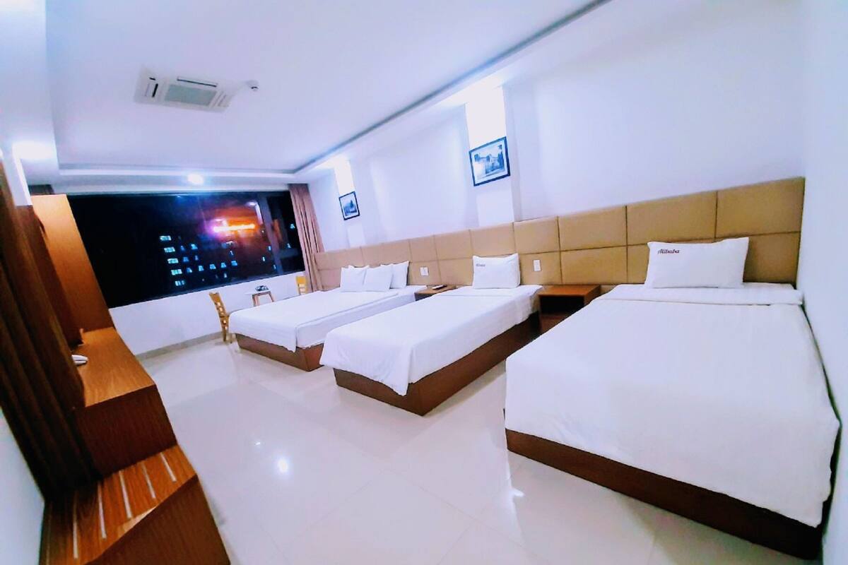 A hotel room with two single beds, a large bed, a desk, and a window with a city view.
