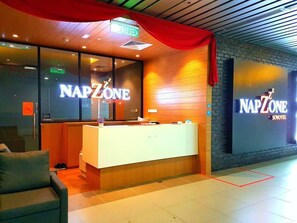 A reception area with a counter, a red curtain, and a sign that reads "NAPZONE". - Napzone KKIA by Sovotel (Kota Kinabalu)