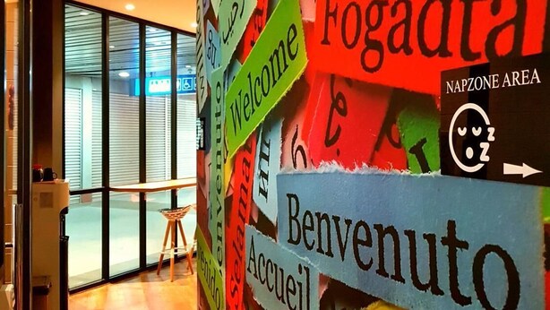 Una pared con letreros de bienvenida en varios idiomas y un cartel que indica una zona de descanso.