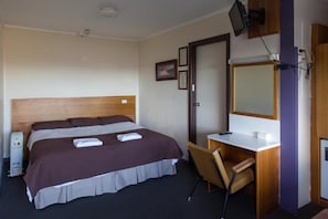 A hotel room with a bed, a desk, a chair, a television, and a door. - Snowy Valley - Hostel (East Jindabyne)