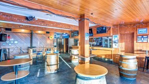 A rustic bar area with wooden barrels as tables, a counter with a menu, and a wooden ceiling. - Snowy Valley - Hostel (East Jindabyne)