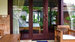 A wooden bench and table outside a building with a glass door, surrounded by plants and a tiled floor. - Villa Sahabat (Gili Trawangan)