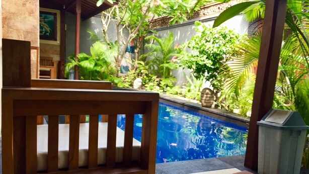 A wooden bench in a tropical garden with a pool. - Villa Sahabat (Gili Trawangan)