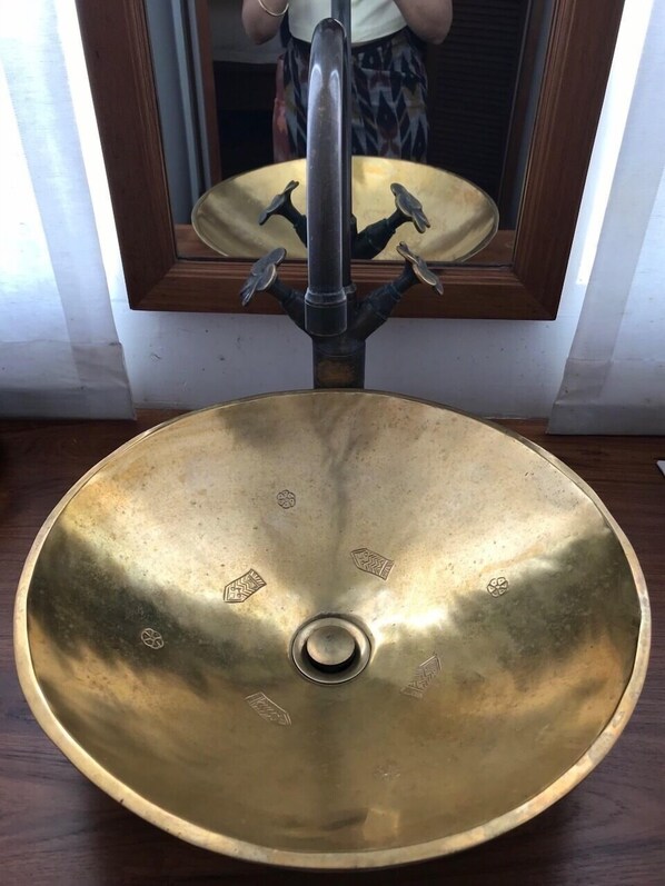 Uma pia de latão com design único, um espelho acima e piso de madeira.
