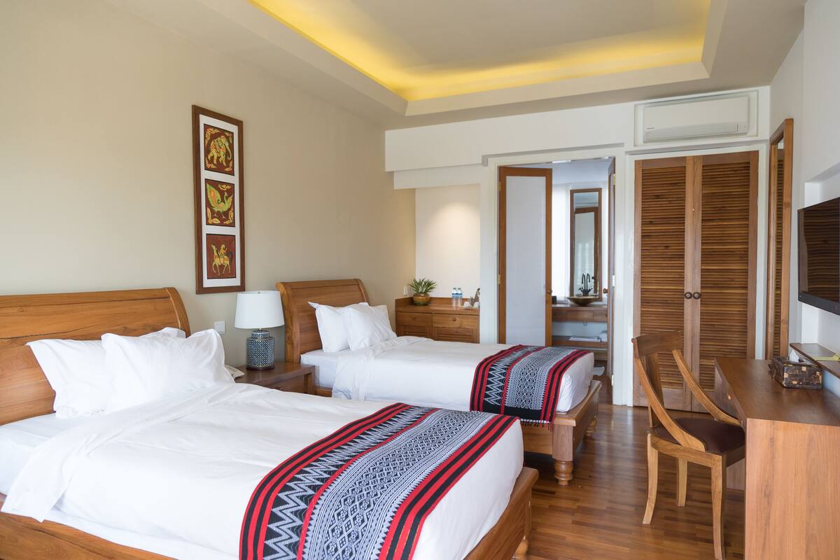 A hotel room with two beds, wooden headboards, a desk with a chair, a television, and a mirror.