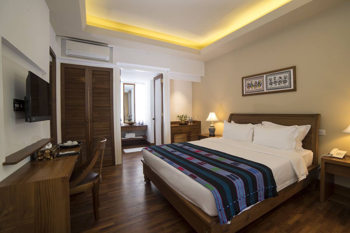 A hotel room with a bed, bedside lamps, a desk, a television, and a bathroom visible through an open door.