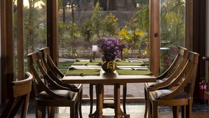 A dining area with a table set for two, featuring wooden chairs and a vase with purple flowers.