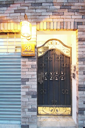 A brick building with a metal gate, a number sign '20 Macchiato', and a light fixture above the gate. - Macchiato (Tainan)