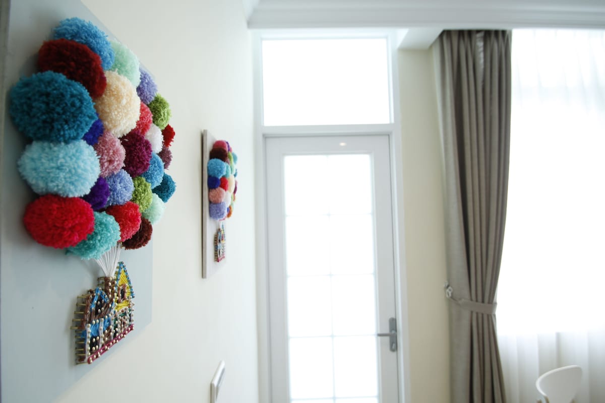 A room with a white door, a window with curtains, and a wall decorated with colorful pom-poms.