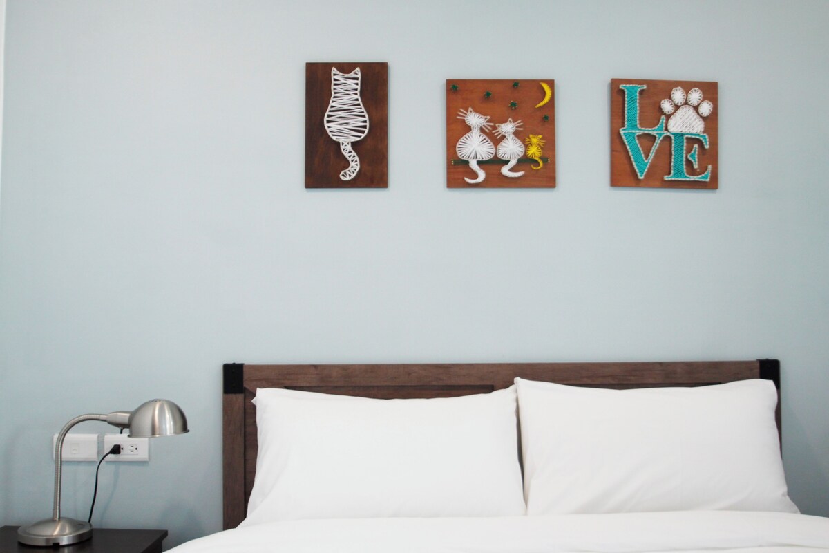 A bedroom with a bed, a nightstand, and three wall art pieces depicting a cat, a dog, and the word "LOVE".