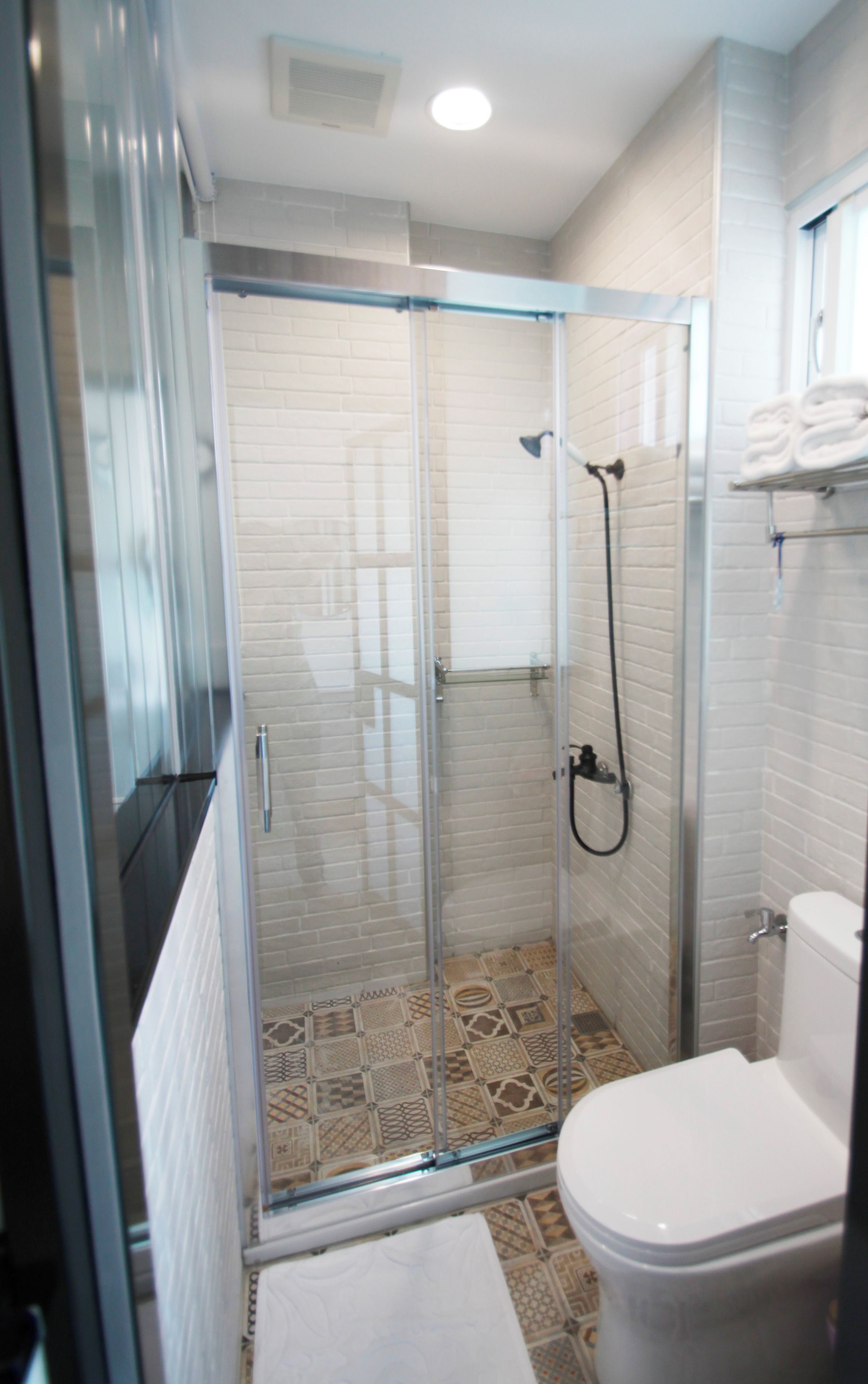 Un baño moderno con ducha envuelta en vidrio, inodoro blanco y baldosas de suelo estampadas.