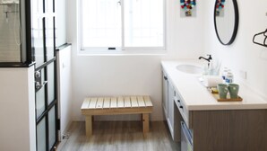 Une salle de bain moderne avec un banc en bois, une grande fenêtre, un lavabo et un miroir.