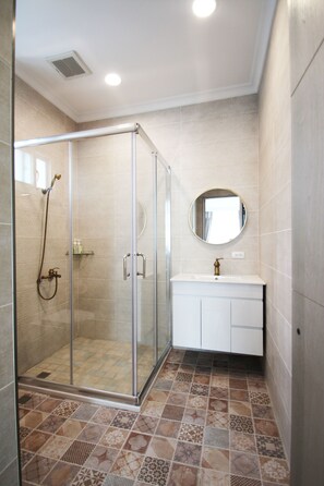 Une salle de bain avec une douche à parois de verre, un miroir rond et un meuble-lavabo blanc.