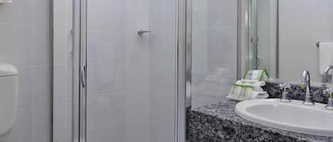 Une salle de bain moderne avec une douche à parois de verre, des toilettes blanches, un lavabo sur un plan de travail en granit et un grand miroir.