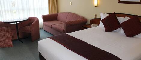 A hotel room with a large bed, a sofa, a small table, and a chair.