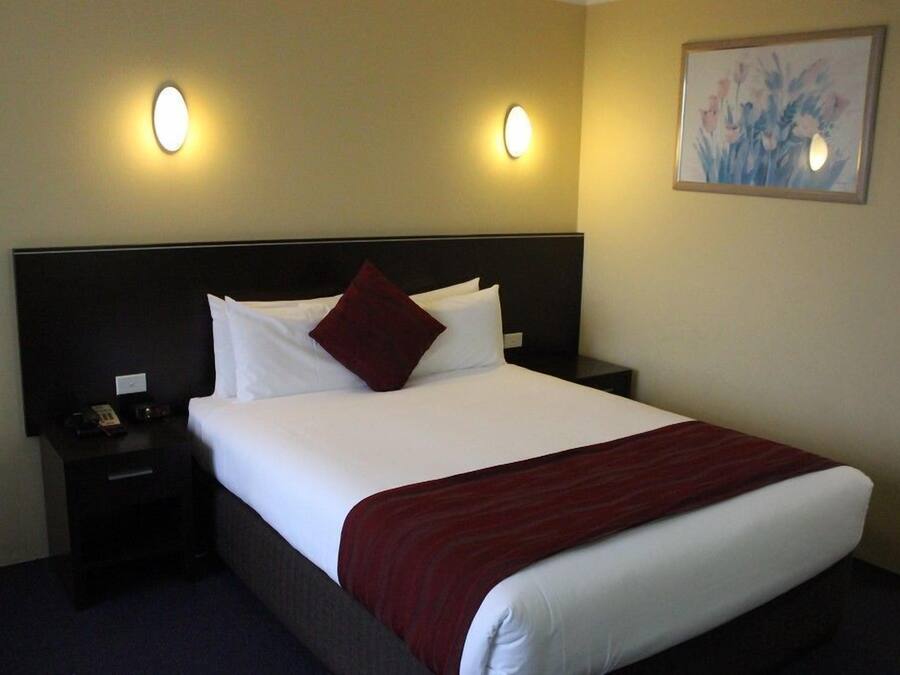 A hotel room with a large bed, two bedside tables, a nightstand, and two wall-mounted lights.