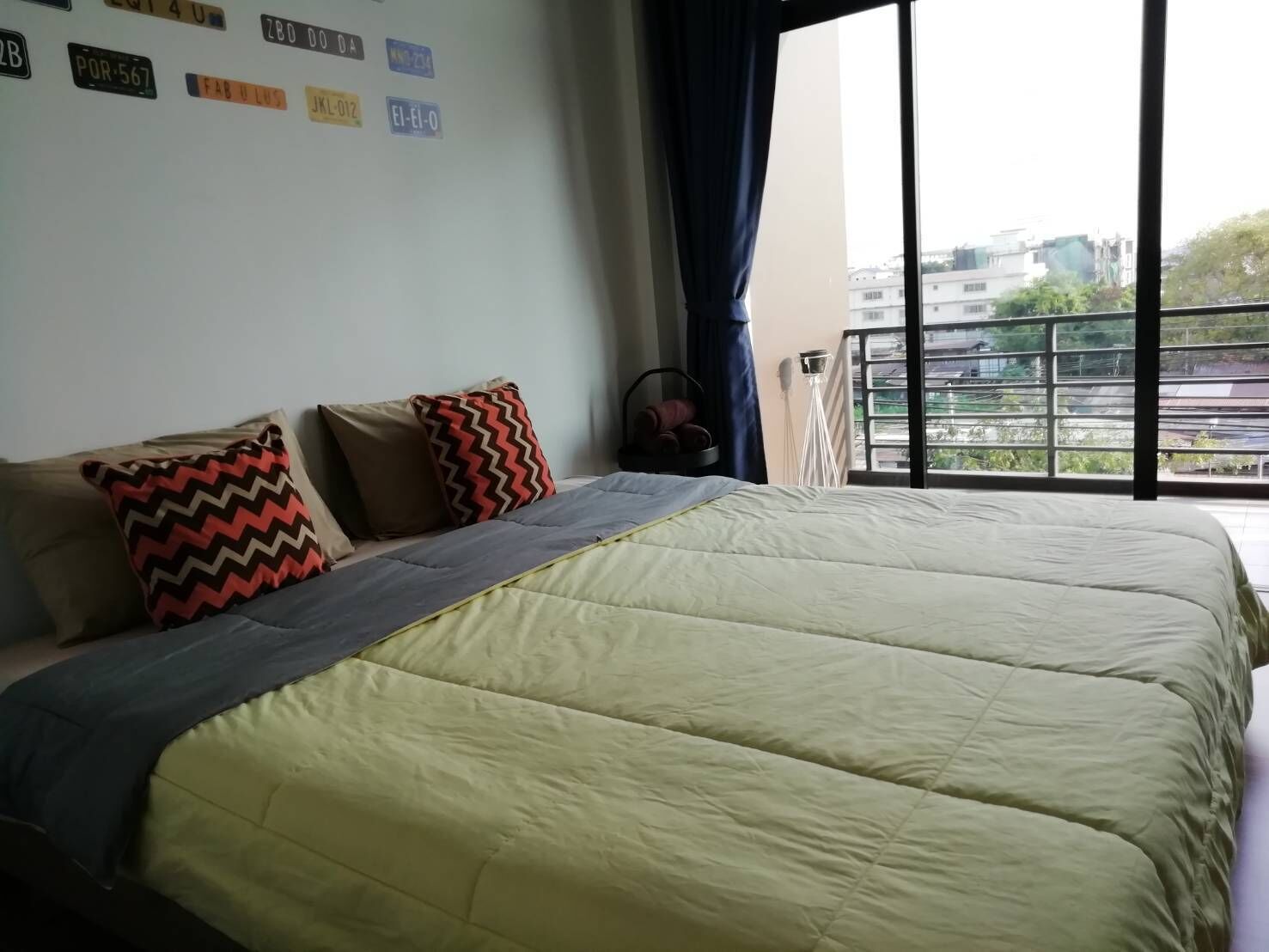 A bedroom with a large bed, a view of the city through a balcony, and a wall with various stickers.