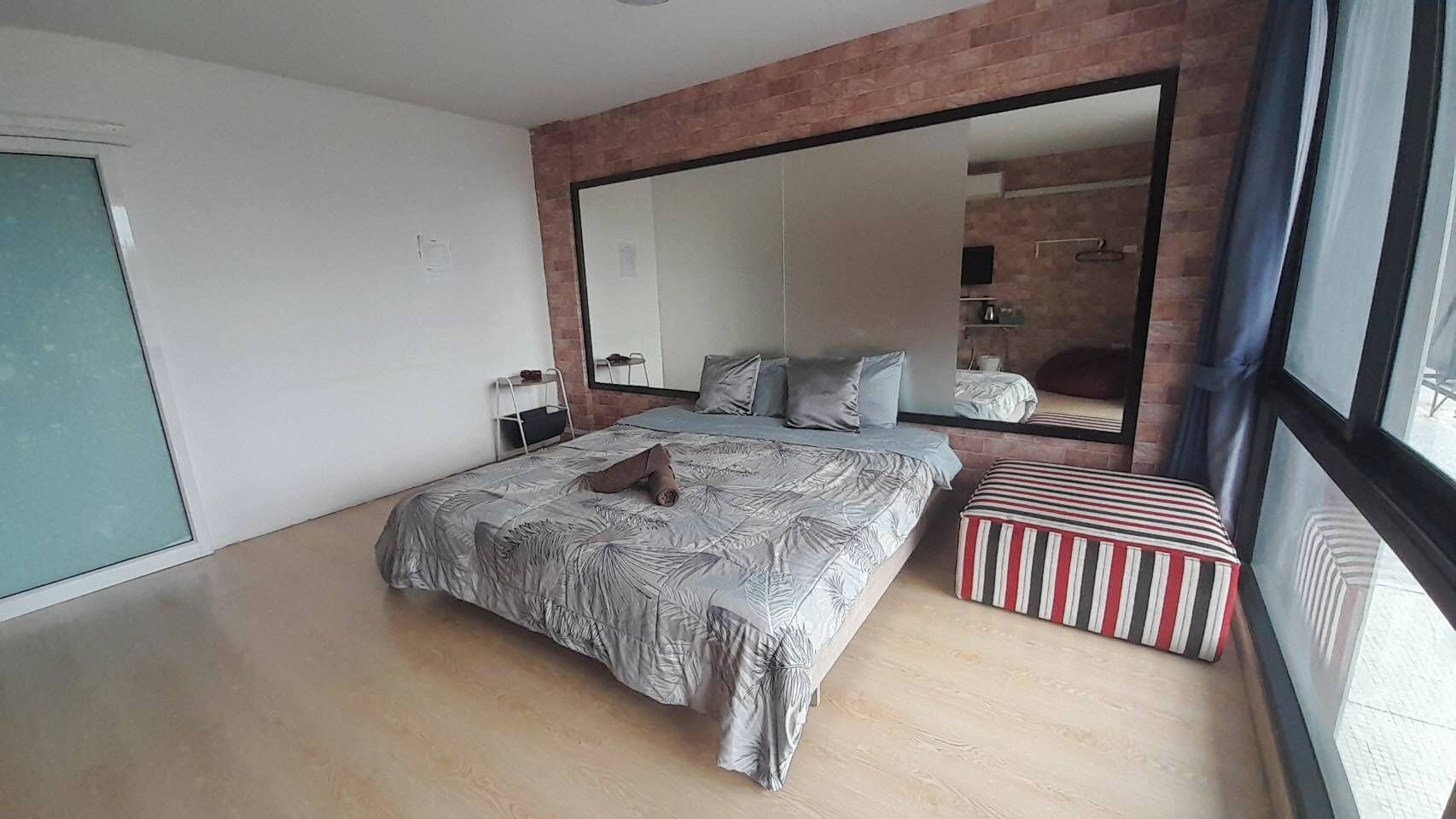 A bedroom with a large bed, a small bedside table, a mirror, and a window with curtains.