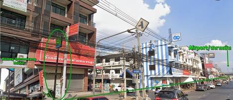 A street view with a hostel named "Homy - Donmueang Hostel" and a sign for "Airport/ Suan Mok."