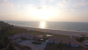 A coastal hotel with multiple buildings, a beach in the background, and a sunset.