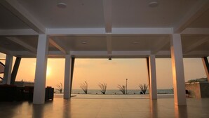 An open indoor space with a view of the sunset over the sea, featuring a modern architectural design with white pillars and a tiled floor.