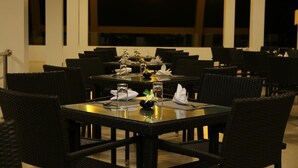 A restaurant with multiple tables and chairs, each set with a glass, napkin, and a small centerpiece.