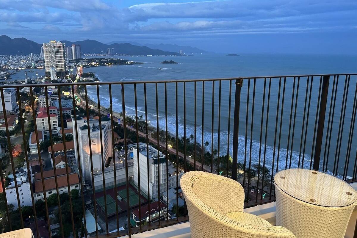 Un balcón con sillas de mimbre que da a una ciudad costera con edificios y una playa.