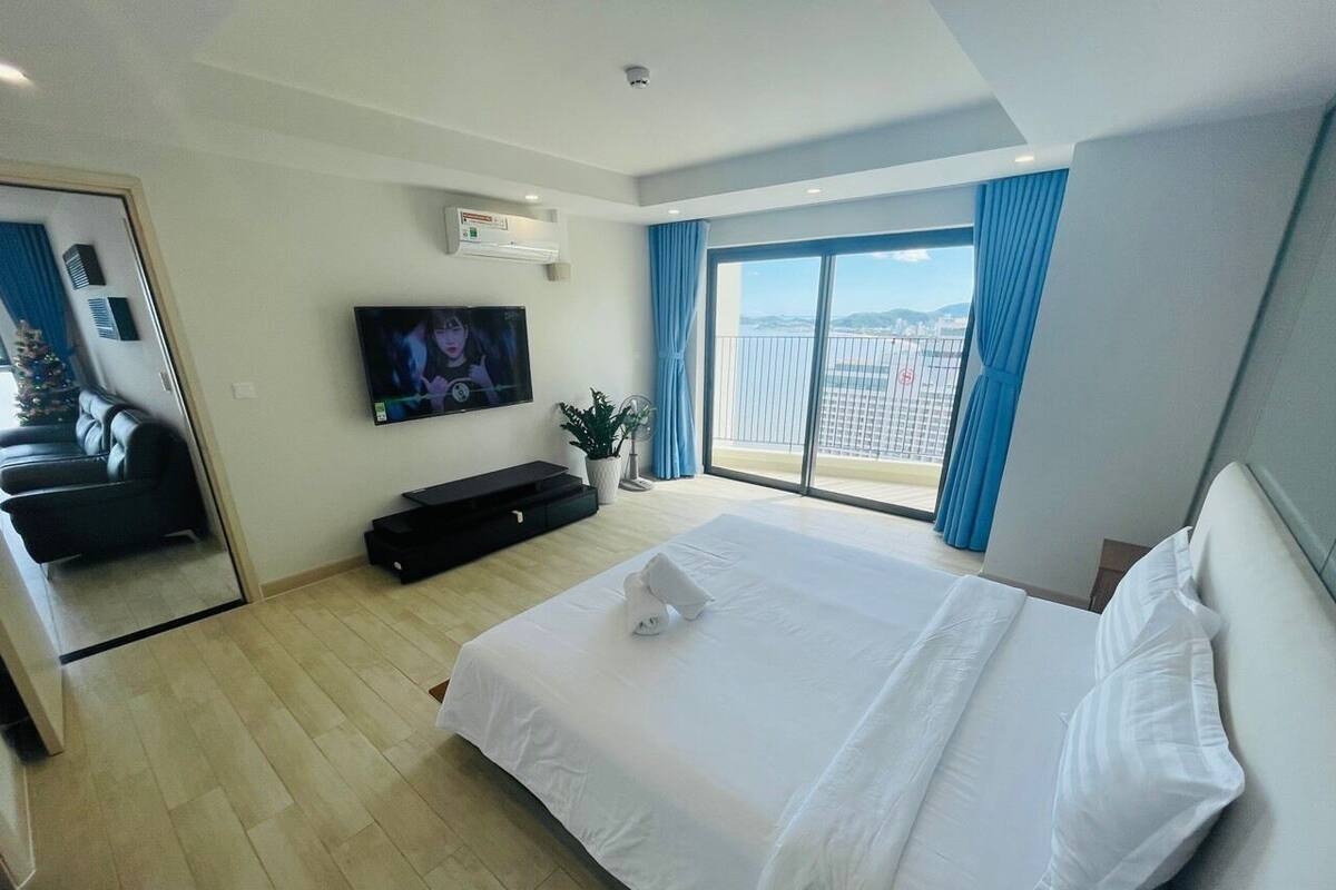 Habitación de hotel con una cama grande, televisión, puerta corredera y vista a la ciudad.