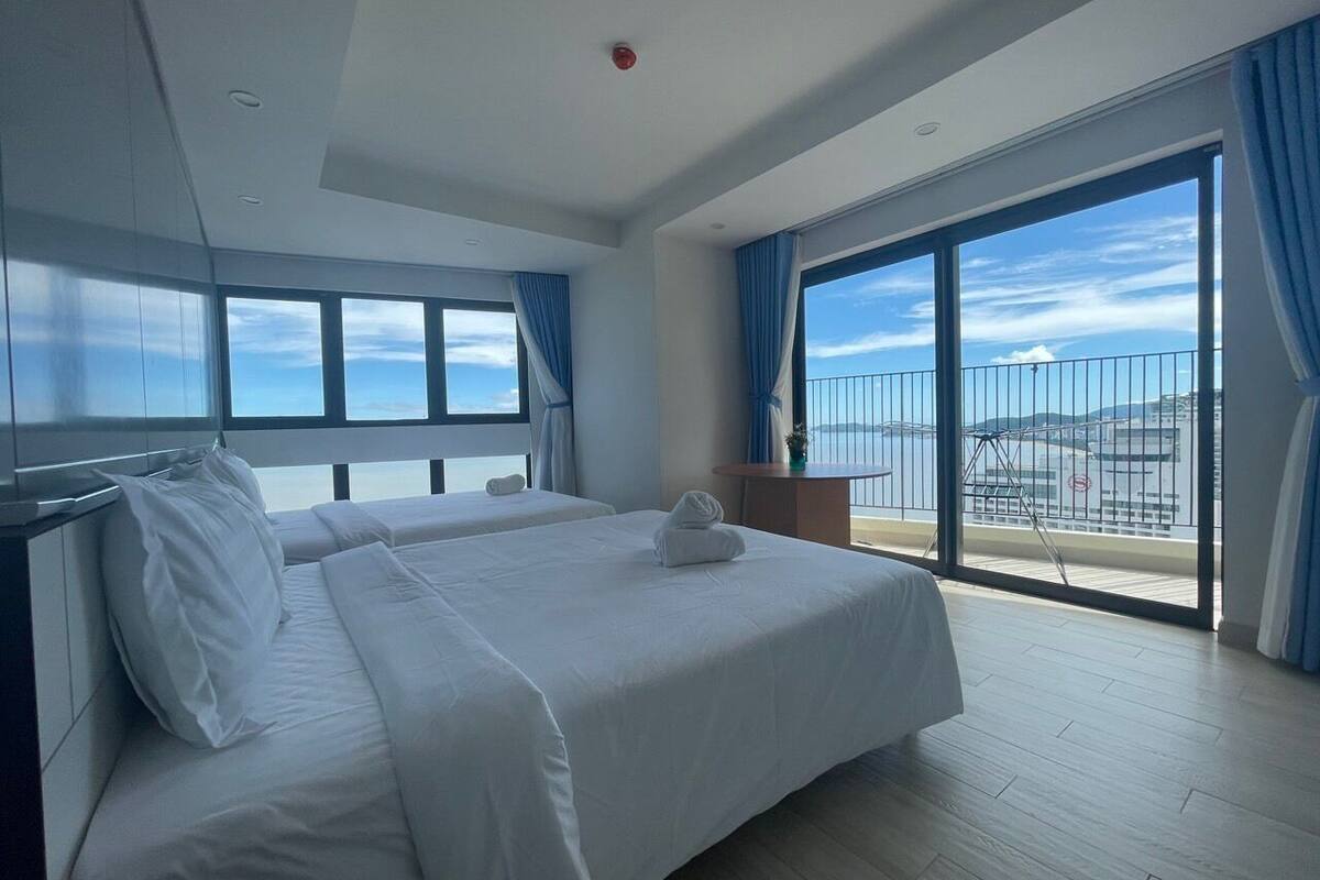 Habitación de hotel moderna con una cama grande, un balcón con vista al mar y una pequeña mesa con una planta.